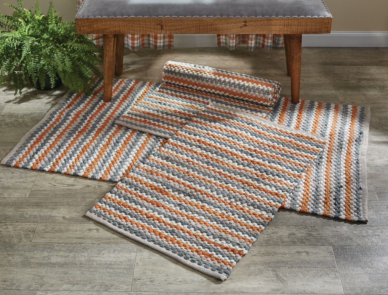 Three orange and gray rag rugs under a bench