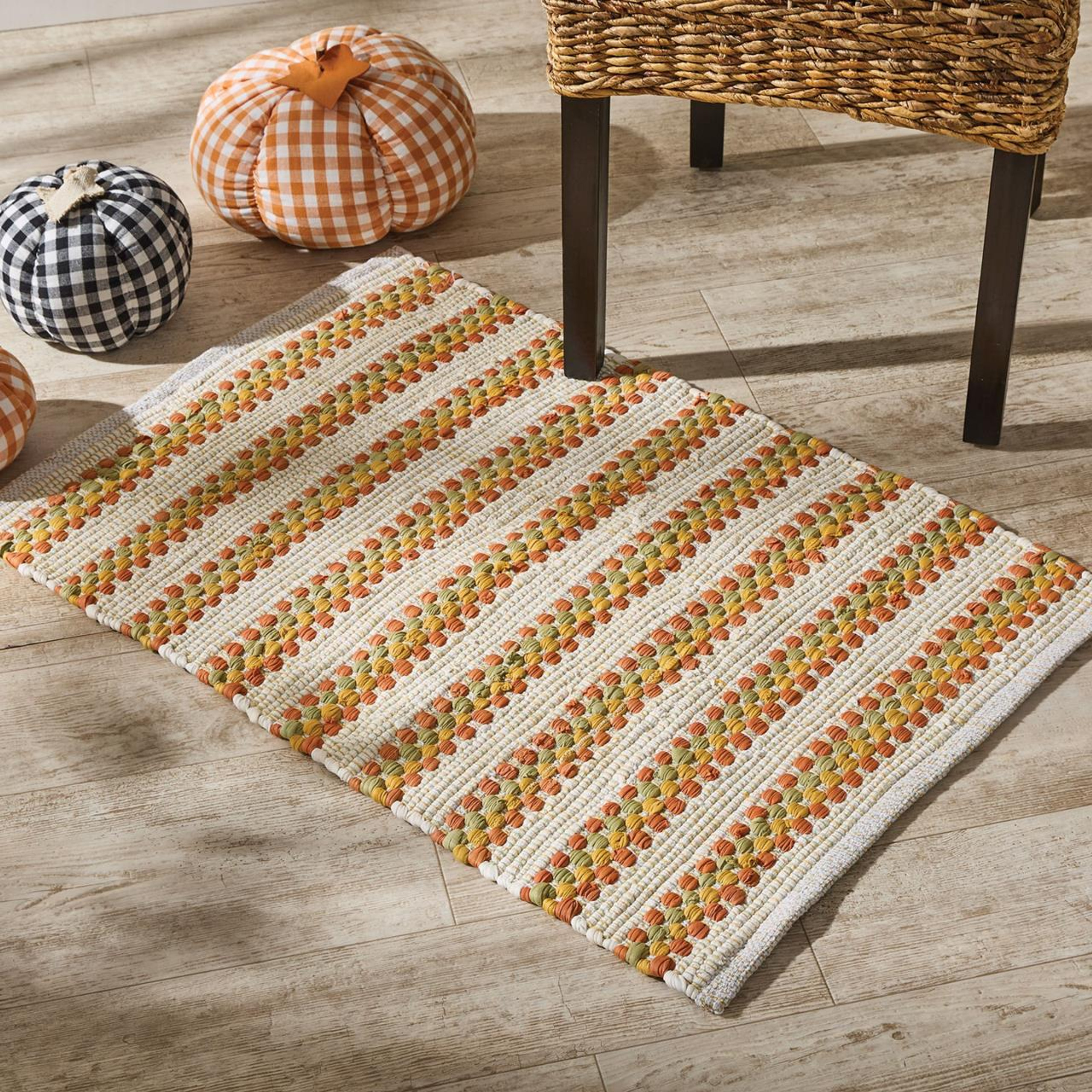 Woven striped orange and white rug on the floor next to plush pumpkins and a chair
