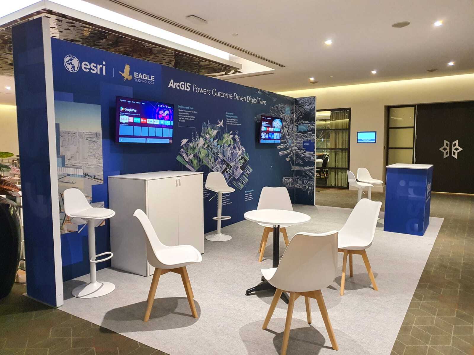 Esri branded conference stand with lounge seating, high stools, screens and full graphic wall in Wellington