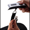 Traveler using digital luggage scale with temperature sensor at airport, weighing a suitcase with ease, highlighting compact design and smart packing convenience.