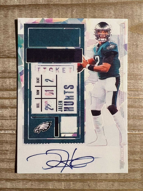 Jalen Hurts 2020 rookie facsimile autograph card displayed on a wooden desk in a plastic sleeve, featuring Philadelphia Eagles colors and printed signature in clear detail
