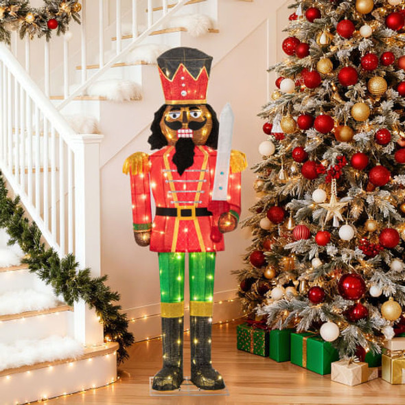 Outdoor Christmas display featuring 5 FT LED Nutcracker with glitter sword illuminating snowy yard at night with warm white lights.