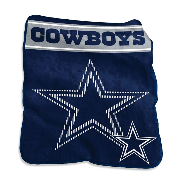 Smiling fan relaxing on a couch wrapped in a large 60x80 Dallas Cowboys Raschel Throw Blanket featuring bold navy blue and silver team logo, showcasing the ultra-soft texture and oversized comfort of the officially licensed NFL product.