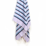 A blue and lilac striped beach towel with fringed ends, hanging against a white background. A blue and lilac striped beach towel with fringed ends, hanging against a white background.