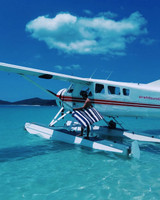 A person stepping onto a float plane while holding a navy and white striped beach towel. The water is clear and blue. A person stepping onto a float plane while holding a navy and white striped beach towel. The water is clear and blue.