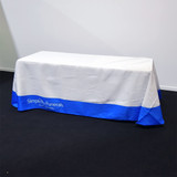 A table covered with a white cloth featuring a blue border and a logo on the front.