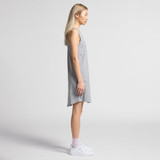 A grey sleeveless dress with a relaxed fit, displayed on a model standing in profile. The model wears white sneakers.