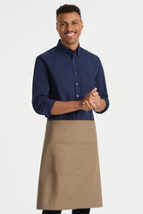A man wearing a navy shirt and a beige waist apron with a front pocket. The apron features a branding logo.