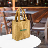 A kraft paper tote bag in a warm brown hue, featuring a logo and sturdy handles, set on a table.
