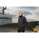 A man's dark grey wool jacket standing at a dock, with a boat in the background and cloudy skies overhead.