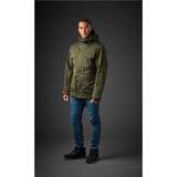 A model wearing a green thermal jacket with a hood, paired with blue jeans and black boots. The jacket features a logo. A model wearing a green thermal jacket with a hood, paired with blue jeans and black boots. The jacket features a logo.