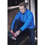 A man in a blue lightweight jacket sits on a bench, adjusting his red running shoes. The jacket has a logo. A man in a blue lightweight jacket sits on a bench, adjusting his red running shoes. The jacket has a logo.