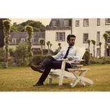 A man sits in an outdoor chair wearing a light blue button-up shirt and dark trousers, with books beside him. A man sits in an outdoor chair wearing a light blue button-up shirt and dark trousers, with books beside him.