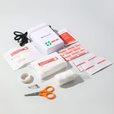 A white waterproof first aid kit containing bandages, adhesive strips, scissors, tape, and a safety pin. A white waterproof first aid kit containing bandages, adhesive strips, scissors, tape, and a safety pin.