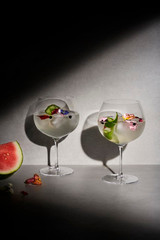A set of two clear gin balloon glasses filled with a cocktail, garnished with mint and edible flowers. A set of two clear gin balloon glasses filled with a cocktail, garnished with mint and edible flowers.