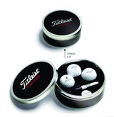 A round black and silver tin containing three white golf balls and a tee, featuring a logo on the lid. A round black and silver tin containing three white golf balls and a tee, featuring a logo on the lid.