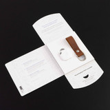 A Tile Pro tracking device in white with a brown vegan leather key fob, presented in an open white package with branding. A Tile Pro tracking device in white with a brown vegan leather key fob, presented in an open white package with branding.