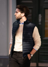 A man wearing a navy puffer vest over a cream sweater, standing outside with a stylish backdrop.