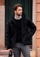A black puffer jacket features a hood, worn over a black sweater, paired with light grey pants and a bag.