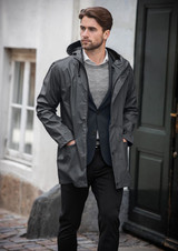 A grey rain jacket with a hood, worn by a man in smart casual attire, standing near a door.