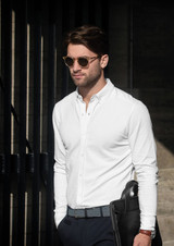 A man wearing a white long-sleeve shirt and sunglasses, holding a black bag.
