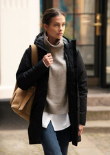 A woman in a black Northdale jacket, wearing a grey sweater and carrying a tan bag, walking outdoors.