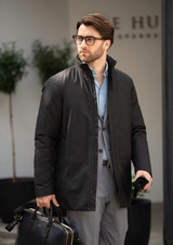 A black men's jacket is worn by a man holding a bag, set in a modern outdoor environment.