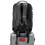 A black backpack with padded straps sits atop a silver suitcase, featuring a branding logo on the front.