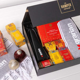 A gift box featuring red and gold packaging, a black bottle, snacks, and festive decorations. Includes logos. A gift box featuring red and gold packaging, a black bottle, snacks, and festive decorations. Includes logos.