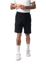 Black men's cotton sandwich shorts with an elastic waistband and side pockets, modelled by a person with tattoos.