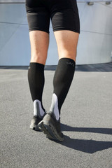 A pair of black compression socks worn with shorts and running shoes, viewed from behind on a textured surface.