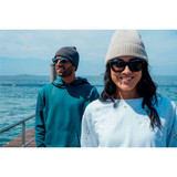 A grey beanie and a cream beanie are worn by two people by the water, wearing sunglasses and casual clothing.