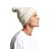 A light cream pom pom beanie worn by a person, featuring a fluffy top and ribbed texture.