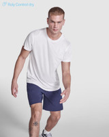 A white Estoril T-Shirt displayed on a model wearing navy shorts. The shirt features a logo.