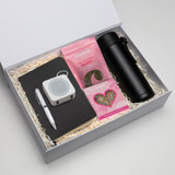A gift box containing a black drink bottle, notebook, pen, speaker, and pink chocolate snakes.