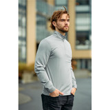 A man wearing a light grey 1/4 zip pullover, standing outdoors with a modern building in the background.