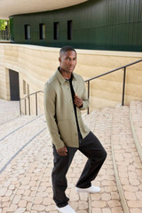 A unisex shirt jacket in olive green, featuring a logo, displayed on a man standing on outdoor steps.