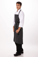 A black and white striped chef apron worn over a white shirt, featuring a logo and paired with black pants and shoes.