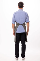 A grey Corvallis Bib Apron worn by a person facing away, paired with a blue shirt and dark jeans.