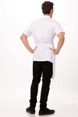 A white bib apron worn by a person, featuring short sleeves and tied at the back, paired with black pants and shoes.