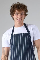 A navy blue bib apron with white vertical stripes, worn by a smiling young man with curly hair.