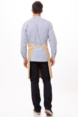 A man is wearing a beige Austin Bib Apron over a checked blue shirt, viewed from the back.