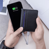 A black recycled leather wallet held in hands, with a phone displaying a charging indicator alongside it.