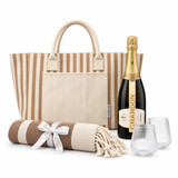 A striped tote bag, a bottle of champagne, two glasses, and a rolled blanket with a ribbon.
