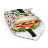 A reusable food wrap featuring a colourful fruit and vegetable pattern, holding a sandwich inside.