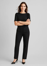 A woman wears black comfort wool stretch relaxed pants paired with a black top and high heels, standing confidently.