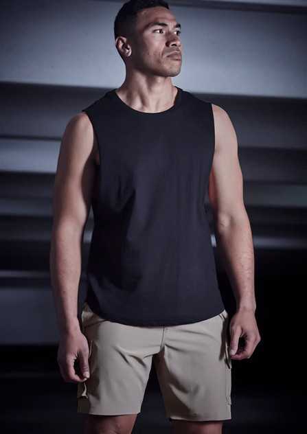 A man wearing a black sleeveless top and beige sports shorts stands in a dimly lit setting. The shorts feature a logo. A man wearing a black sleeveless top and beige sports shorts stands in a dimly lit setting. The shorts feature a logo.