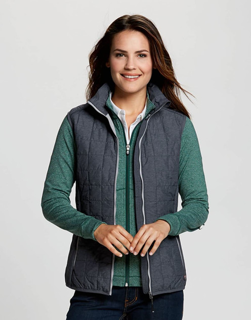 A woman wears a grey puffer vest over a green top, featuring a branding logo on the vest. A woman wears a grey puffer vest over a green top, featuring a branding logo on the vest.