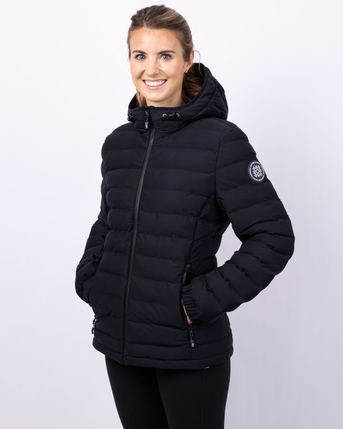 A black puffer jacket with a hood, featuring a logo on one sleeve, worn by a smiling woman. A black puffer jacket with a hood, featuring a logo on one sleeve, worn by a smiling woman.