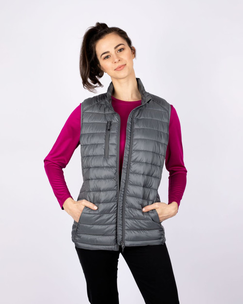 A grey padded vest with a high collar, featuring front pockets and a zip closure, worn over a pink long-sleeve top. A grey padded vest with a high collar, featuring front pockets and a zip closure, worn over a pink long-sleeve top.